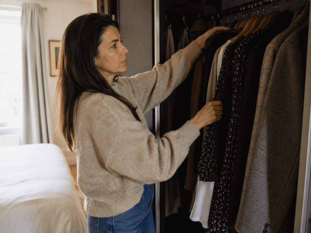 Woman pulling unworn clothes from the back of her wardrobe for a personal style test.
