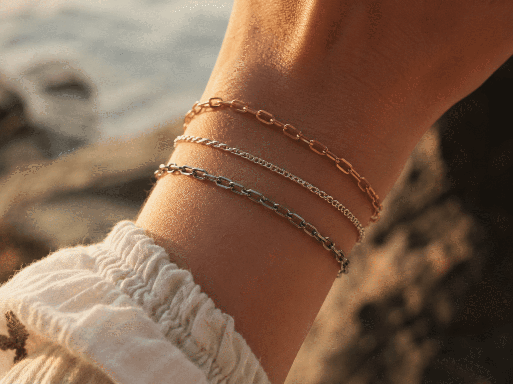 A woman’s wrist wearing three layered bracelets in warm golden hour light with a soft blurred background.